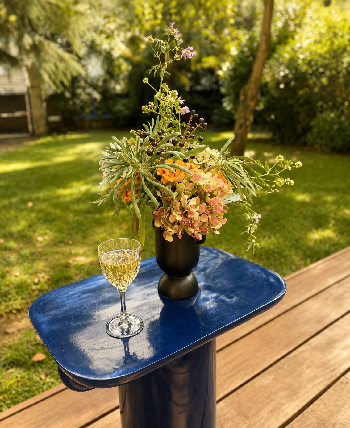 Bouquet champêtre et verre de vin blanc sur le guéridon bleu, au jardin