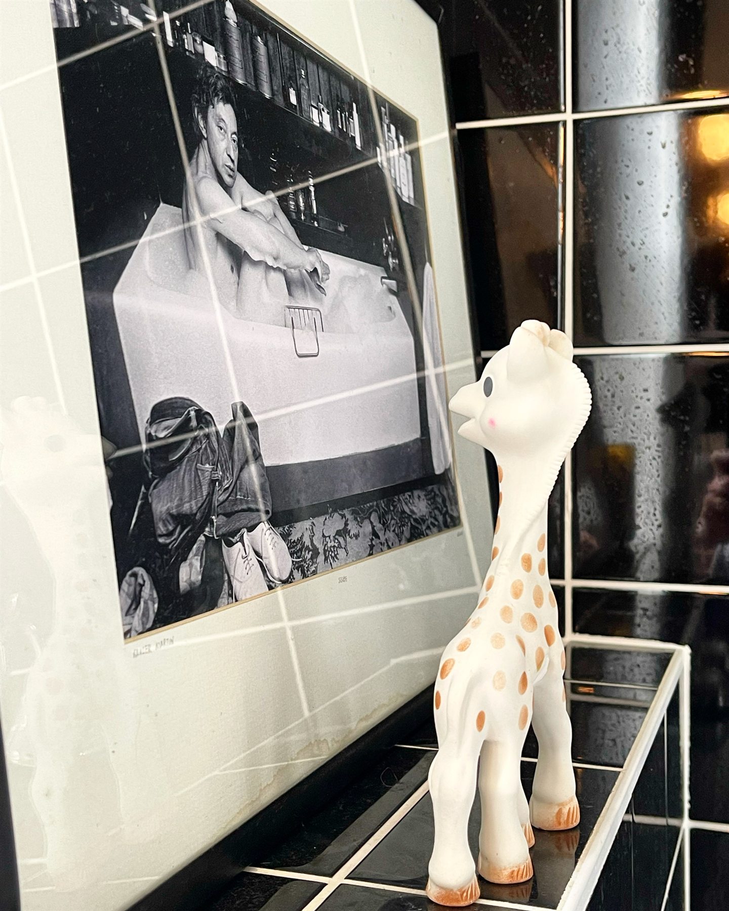 Sophie la girafe devant une photographie en noir et blanc, dans la salle de bain